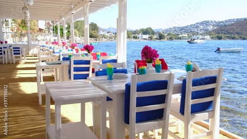 Aegean fish restaurant, tables and chairs with bougainvillea flowers next to see in Bodrum, Turkey at sunny day. It is very famous and attraction point for tourist in Bodrum.
