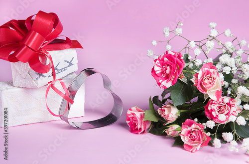 Fototapeta Naklejka Na Ścianę i Meble -  Decorative metal heart, red rose bouquet and gift box, greeting card on pink background. Holiday congratulations concept.