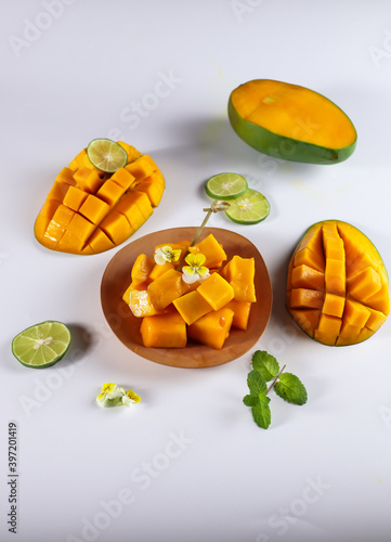 Mangga or Mango ripe with nicely cut pieces on a wooden plate garnish wit viola, lime and mint leaf on white background.