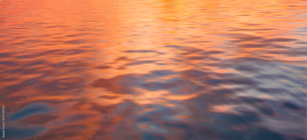 A beautiful sunset over the calm sea with red and orange clouds reflecting in the water