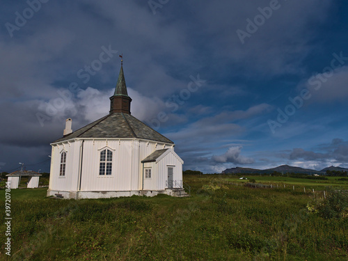 Historic wooden church constructed in octagonal style with white painted facade between green meadows near village Dverberg on Andøya island, Vesterålen,Norway on sunny day in late summer with clouds.