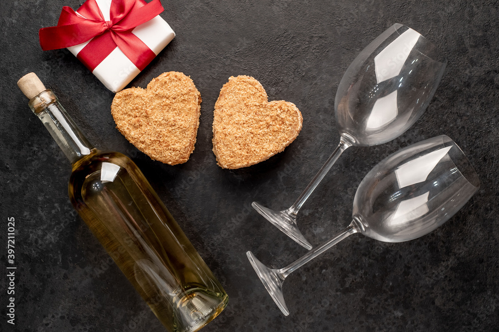 A festive dinner for two on Valentine's Day. Heart shaped cakes and white wine bottle with glasses, gift on stone background A festive dinner for two on Valentine's Day. Heart shaped cakes and white wine bottle with glasses, gift on stone background