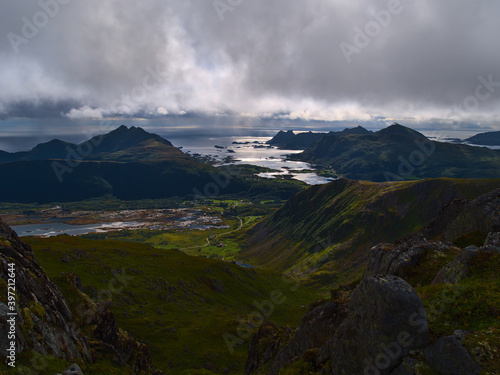 Panoramic view of the south of Vestvågøy island, Lofoten, Norway with Finnstadpollen fjord and rugged mountains covered by green grass viewed from Justadtinden on summer day with unsettled weather.