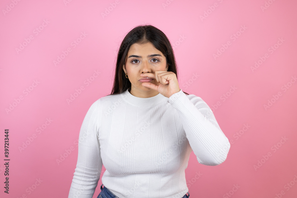 Young beautiful woman over isolated pink background mouth and lips shut as zip with fingers. Secret and silent, taboo talking Young beautiful woman over isolated pink background mouth and lips shut as zip with fingers. Secret and silent, taboo talking