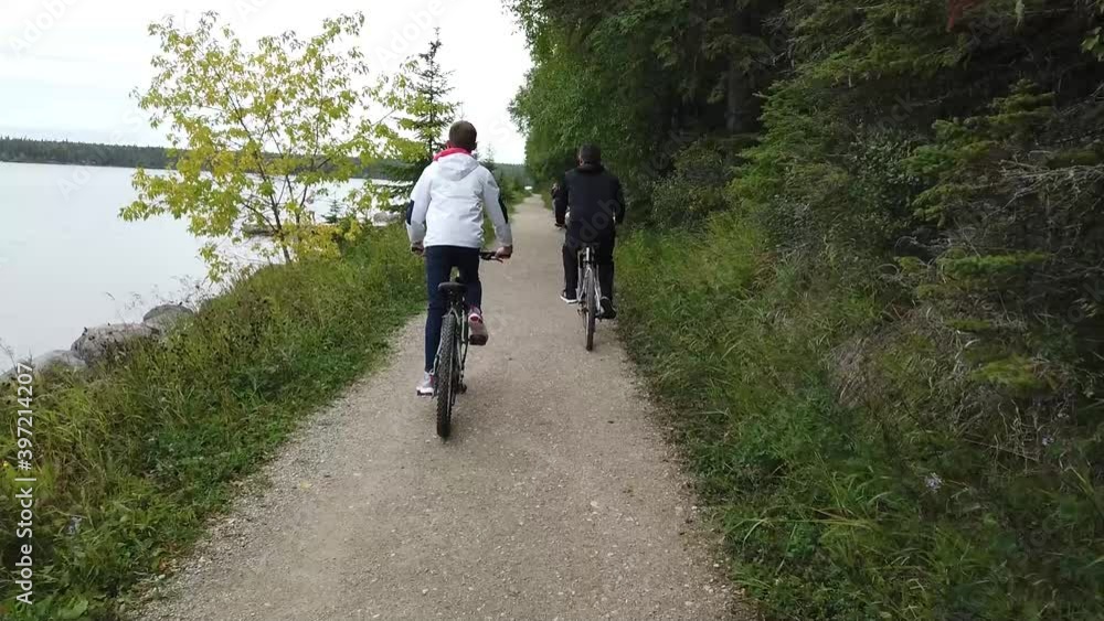 Slow motion clip of two bikers riding on a gravel trail next to a lake. Outdoors, summertime, overcast. Mid-shot. Slow motion clip of two bikers riding on a gravel trail next to a lake. Outdoors, summertime, overcast. Mid-shot.