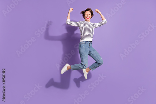 Full length photo of cute lucky young woman wear casual outfit jumping rising fists isolated violet color background