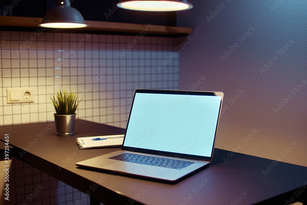 Fototapeta premium Workspace for remote online work at a laptop with empty white screen mockup in a modern loft interior