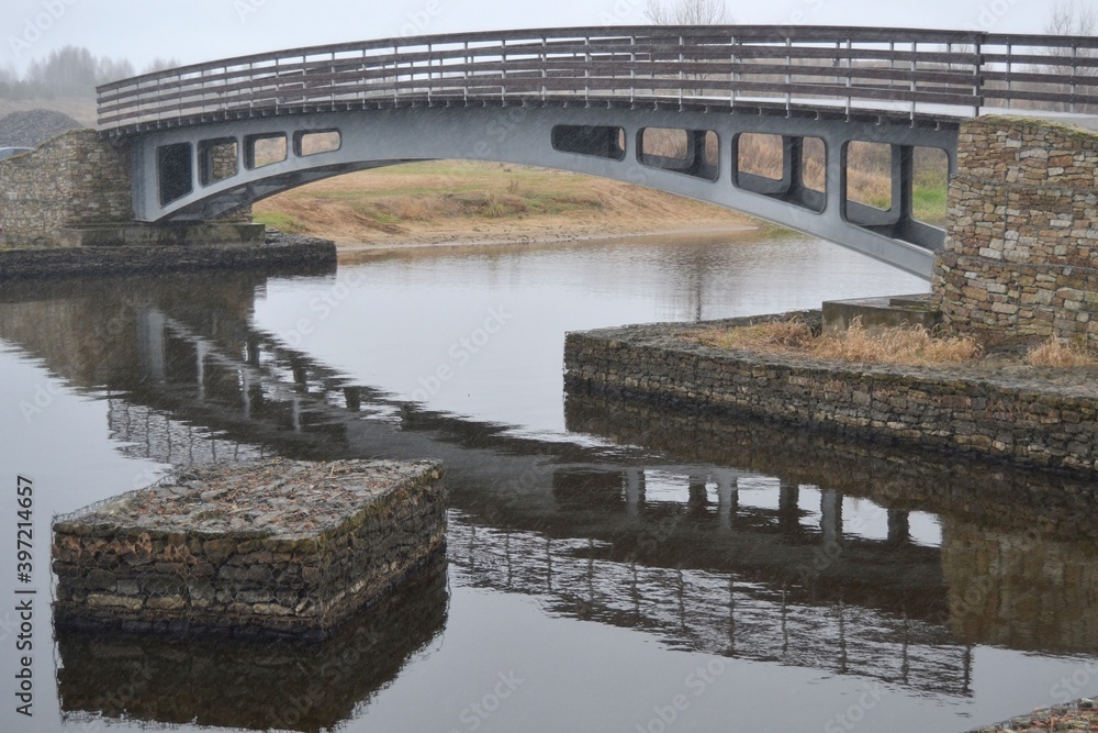 Fototapeta premium Modern metal pedestrian bridge across the river on a stone foundation.