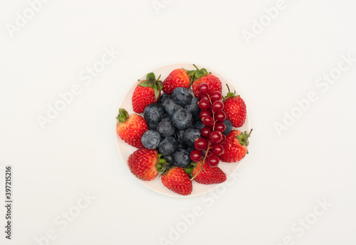 Various fresh summer berries  strawberries  currant  blueberries on white plate on white background. Summer time concept. Vitamins  healthy eating  harvest. Selective focus. Flat lay style.