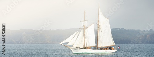 Tableau sur toile An elegant two-masted gaff schooner (tall ship) near the rocky shores of Brittany, France