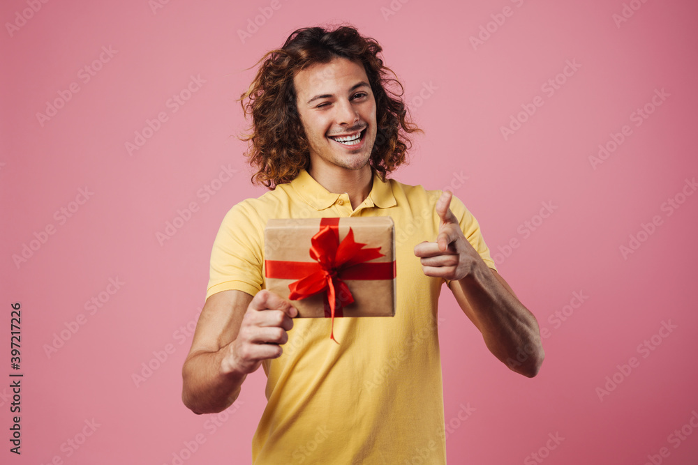 Happy guy winking and pointing finger at camera while showing gift box Happy guy winking and pointing finger at camera while showing gift box