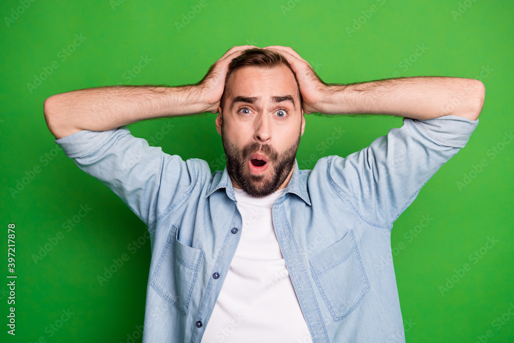 Portrait of impressed sad man wear blue shirt arm head open mouth isolated on green color background Portrait of impressed sad man wear blue shirt arm head open mouth isolated on green color background