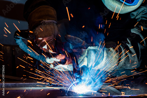 Cuadro en lienzo Employee welding steel with sparks using mig mag welder - focus on sparks
