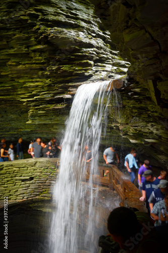People walk quickly, so they don't get soaking wet, behind a falls on the Gorge Trail at Watkins Glen State Park in Upstate NY.
