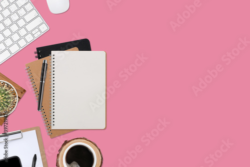 Top view pink wooden workspace office desk with computer and office supplies. Flat lay work table with blank notebook, keyboard, green cactus and coffee cup. Copy space for your advertising content.