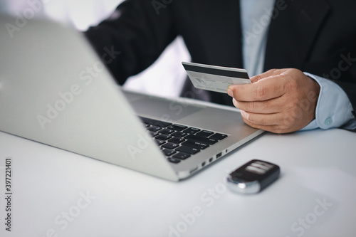 Man hands in black suit sitting and holding credit card and using smartphone on table for only monthly car payment or shopping online. Businessman using laptop computer.