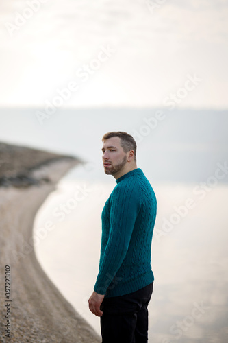 Portrait of a young man in a turquoise sweater standing by the river