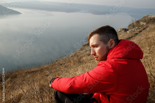 Portrait of a man who looks into the distance and sits in the grass by the river