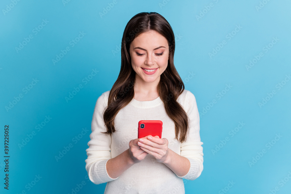 Photo of adorable sweet wavy lady wear white sweater holding looking modern device isolated blue color background Photo of adorable sweet wavy lady wear white sweater holding looking modern device isolated blue color background