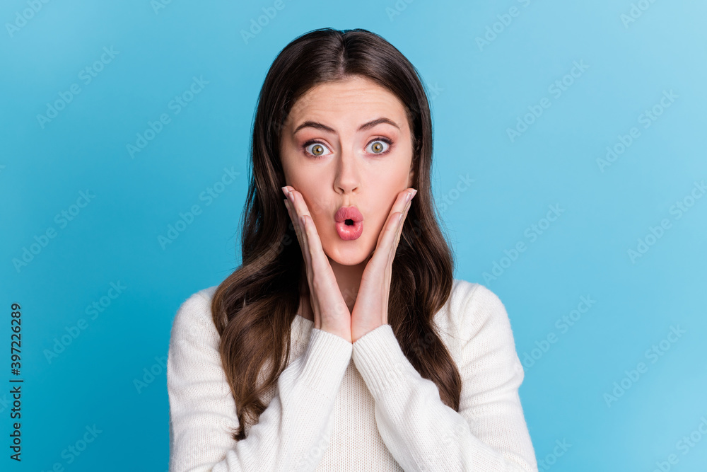 Photo of shocked shiny curly woman dressed white pullover big eyes arms cheeks isolated blue color background Photo of shocked shiny curly woman dressed white pullover big eyes arms cheeks isolated blue color background