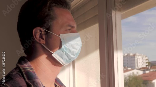 Middle aged man on the balcony of the house during the covid-19 outbreak lockdown. male with medical mask, worried and tired face looking at the street depressed in quarantine. Isolation concept