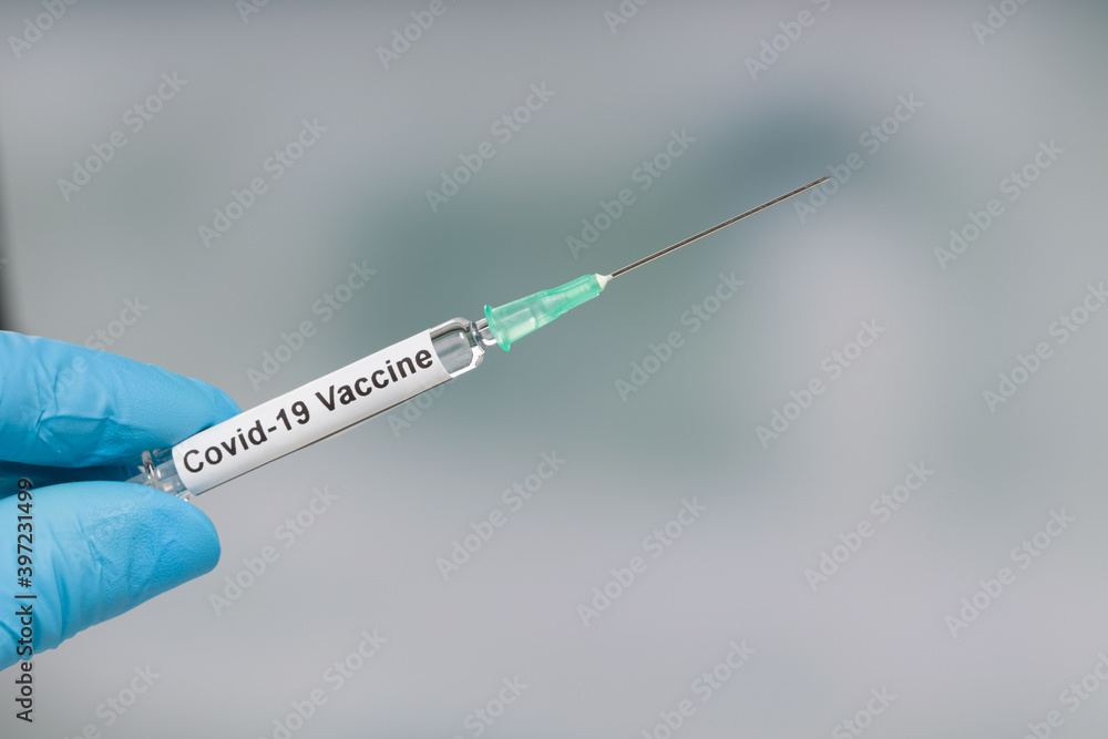 Close up of scientist's or doctor's hand in medical gloves with a syringe containing a Covid-19 serum / vaccine Close up of scientist's or doctor's hand in medical gloves with a syringe containing a Covid-19 serum / vaccine