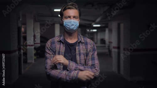 Man auto mechanic wearing protective face mask while standing with arms crossed in a workshop. Male portrait during coronavirus pandemic in garage, small business owner