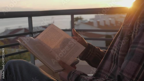 Middle aged man reading book on sunset, freelancer on balcony read during home isolation, coronavirus covid 19 lockdown, remote learning