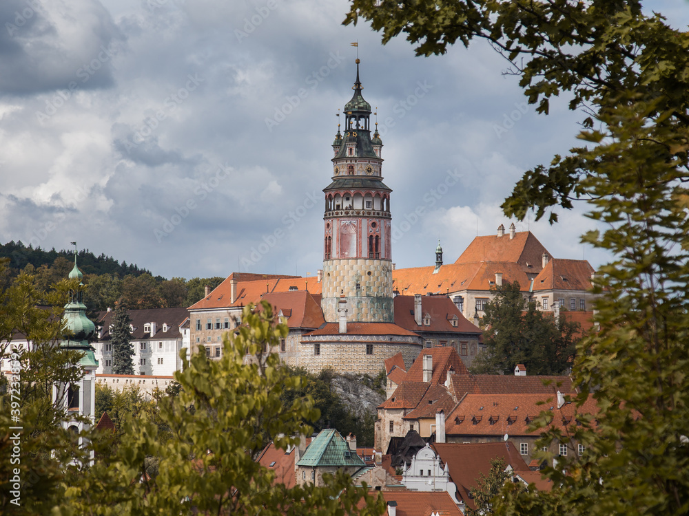 Rooftop view to Cesky Krumlov town. Triangle orange roofs and beautiful bell tower. Cloudy sky, green foliage. No people Rooftop view to Cesky Krumlov town. Triangle orange roofs and beautiful bell tower. Cloudy sky, green foliage. No people