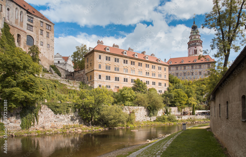 Panorama view to Cesky Krumlov town. Triangle orange roofs and beautiful bell tower. Cloudy sky, green foliage. No people