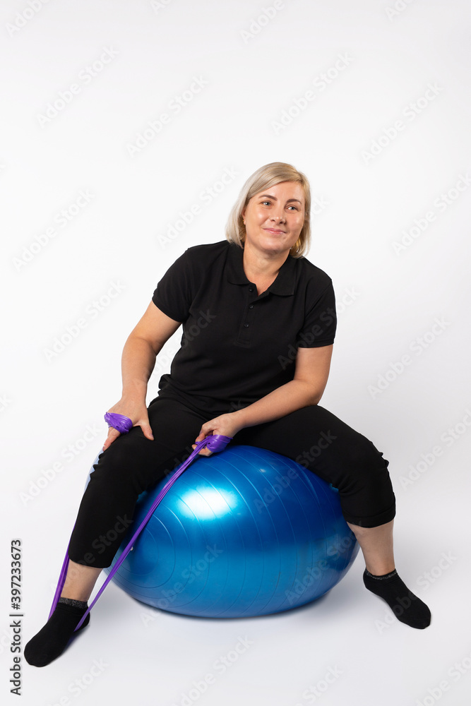 Senior woman doing exercises on a fitness ball and with an elastic band. Photo on a white background. Senior woman doing exercises on a fitness ball and with an elastic band. Photo on a white background.