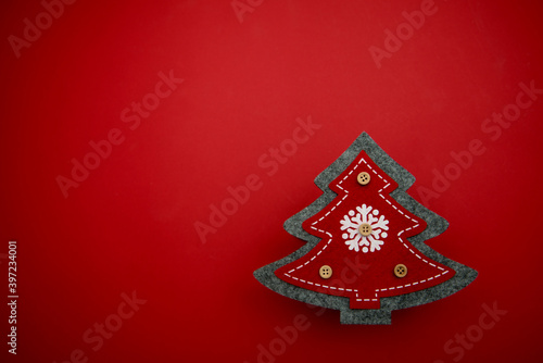 Christmas tree gray with red sewn fabric with a white snowflake in the center and with buttons on a red background. Christmas tree made of fabric on a red background with buttons
