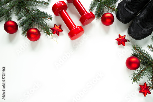 Two red dumbbells, training shoes, Christmas tree branches, decorative baubles ornaments. Healthy lifestyle Holiday season composition, festive flat lay concept with copyspace on white background.