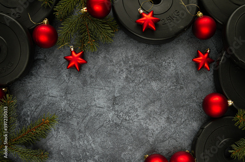 Heavy dumbbells weight plates and Christmas tree branches with decorative baubles ornaments. Healthy lifestyle Holiday season composition, festive flat lay concept with copyspace.