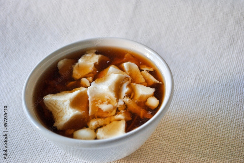 Tofu pudding with dark brown sugar (Moscuvado) syrup in white bowl. A popular dessert in South East Asia. Close up. Life style. Tofu pudding with dark brown sugar (Moscuvado) syrup in white bowl. A popular dessert in South East Asia. Close up. Life style.