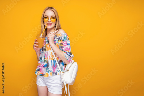 Pretty confident blonde in cap and summer outfit holding drink in cup posing on studio background isolate. © zamuruev