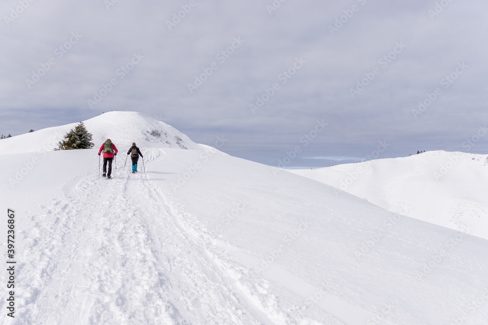 Senior couple is snowshoe hiking in alpine snow winter mountains. Allgau, Bavaria, Germany.