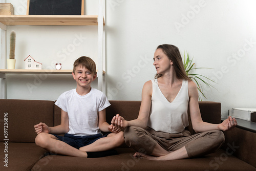 Young mother and child boy doing yoga, meditate in lotus position on couch