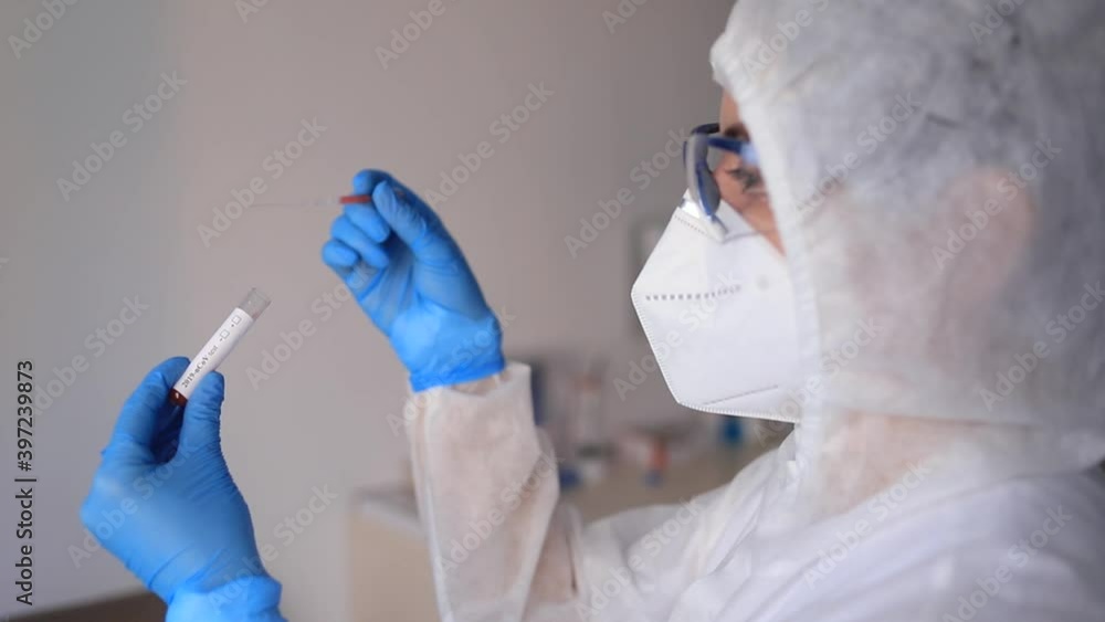 Slowmotion scene of medicine woman wearing protective gear, holding a test tube for 2019-nCoV analyzing. Coronavirus blood test concept. Selective focus Slowmotion scene of medicine woman wearing protective gear, holding a test tube for 2019-nCoV analyzing. Coronavirus blood test concept. Selective focus