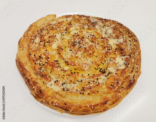 Step 3. Burek with spinach and ricotta cheese. Round pie with cheese, herbs, greased with yolk, sprinkled with sesame seeds. Delicious Balkan pie Borek. Vegetarian baked goods. photo