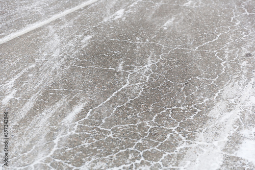 Cracks on the asphalt filled with snow. Low drifting snow on Winter road texture background