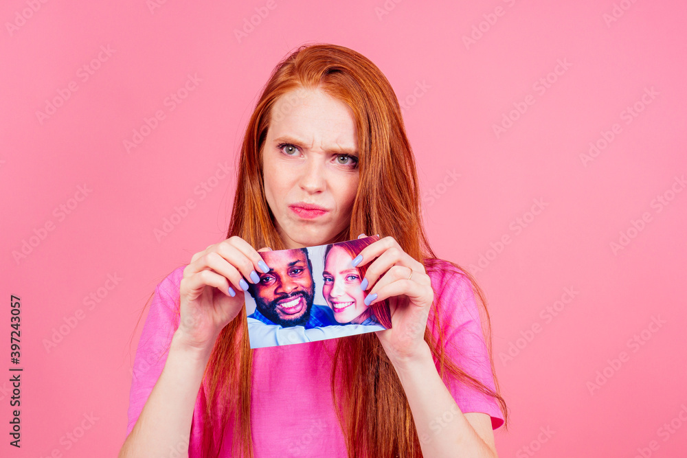 redhaired ginger woman in pink studio background tearing photo card of smiling international couple the end of the relationship redhaired ginger woman in pink studio background tearing photo card of smiling international couple the end of the relationship
