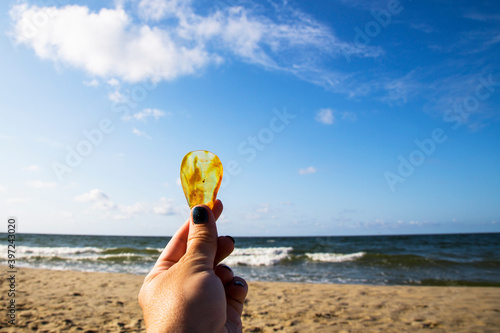 Amber. Very beautiful transparent amber in the palm of your hand. On the sandy beach lies a hand with an amber stone. Bright and transparent amber against a bright blue sky. Frozen wood resin. Baltic