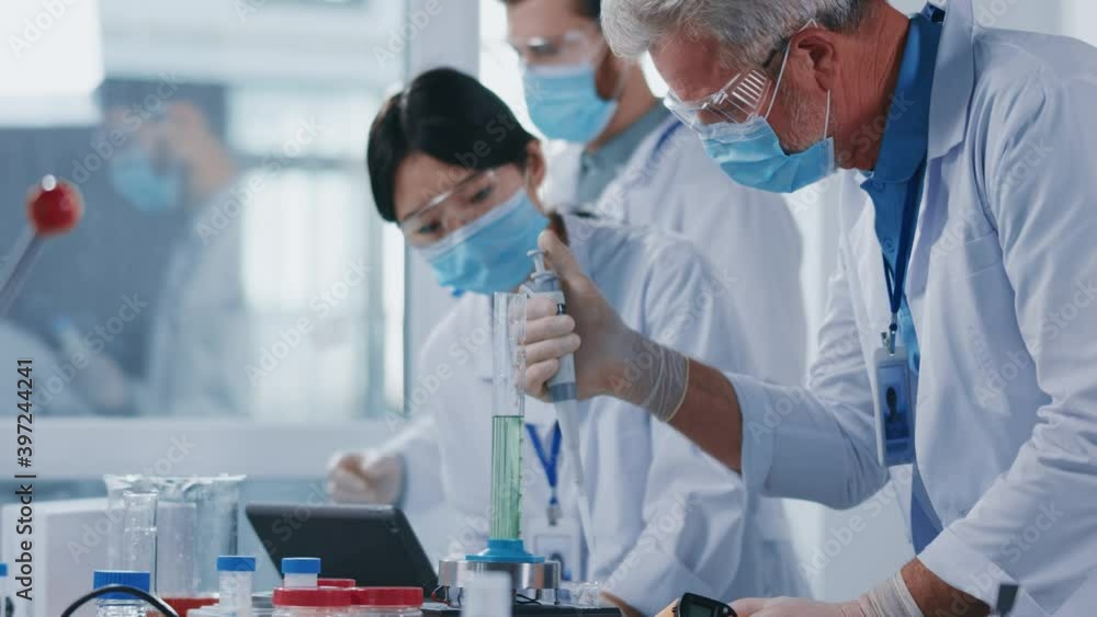 Multi-race diverse team of cooperating scientists with chief mature engineer wearing protective masks processing experiments in medical laboratory. Multi-race diverse team of cooperating scientists with chief mature engineer wearing protective masks processing experiments in medical laboratory.