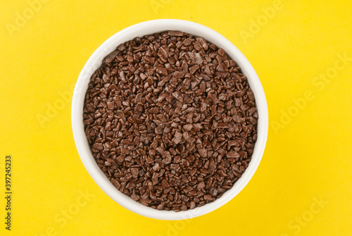 Granulated chocolate in white bowl with yellow background.