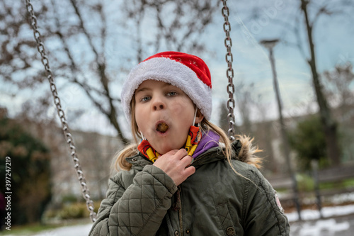Kinder/Jugendlich leiden wegen der Corona-Covid-19 Pandemie unter dem Lockdown. Das Mädchen ist einsam und allein auf dem Kinderspielplatz. Nur zum Naschen darf sie im Park den Mundschutz abnehmen.