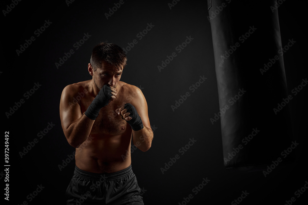 Male boxer punching in boxing bag on black background