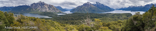 An ultra wide panorama of a cloudy day in the wilderness of Patagonia surrounded by mountains, water and trees seen from Cerro Llao Llao viewpoint
