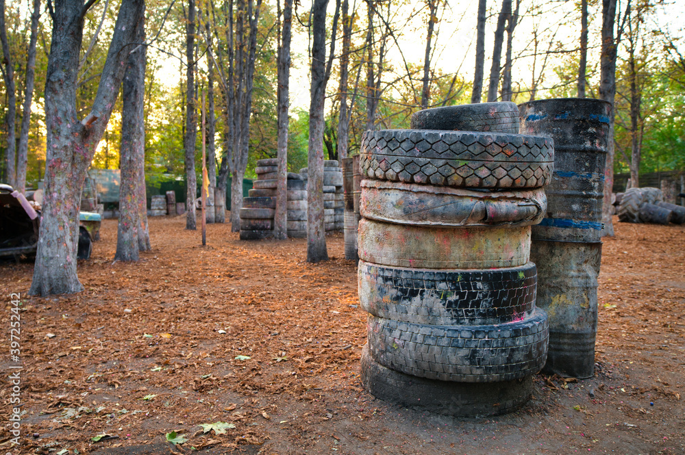 Fototapeta premium Old rusty barrels and damaged tires on a paintball base