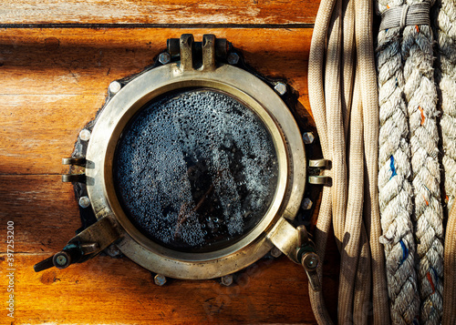 Vintage sailboat brass porthole and ropes on wooden wall. Mist on the glass window.